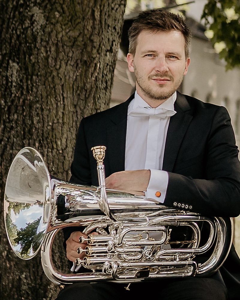 Kevin Van Giel in concertkledij met zijn euphonium, tegen een boom